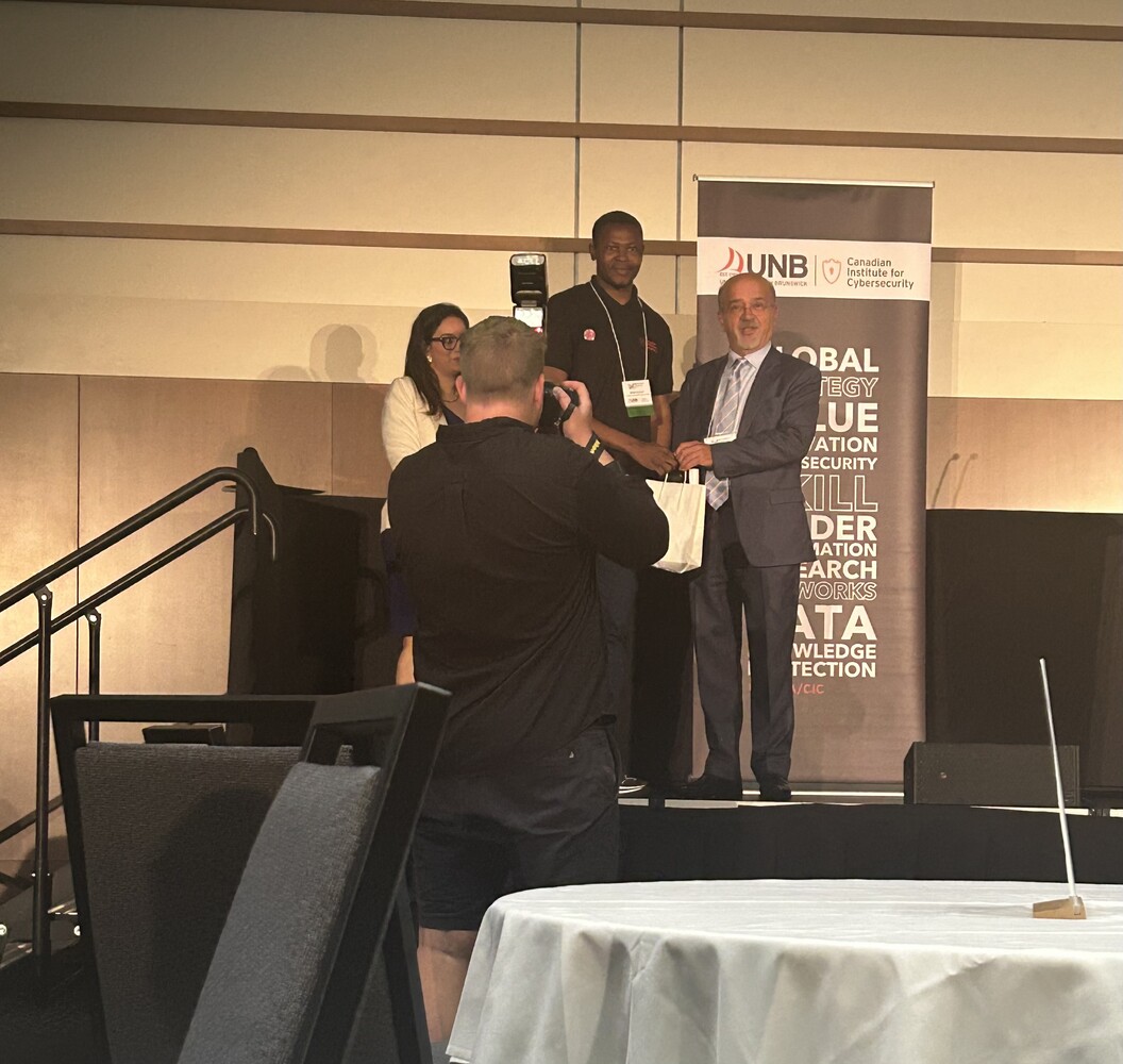 Dr. Ali Ghorbani, Director of the Canadian Institute for Cybersecurity, presenting one of the Best Poster Award to Ogobuchi Daniel Okey for his research poster at the #PST2025 Industry Summit in Fredericton.